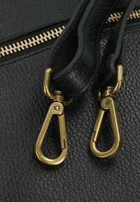 Sac en cuir noir texturé avec des accessoires en métal doré, comprenant deux crochets à pression et une fermeture éclair robuste. Gros plan sur les détails.