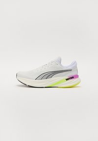 Zapatilla de running blanca con parte superior de malla, detalles en negro y una suela intermedia texturizada. Presenta acentos en rosa y verde neón en el talón y la suela.