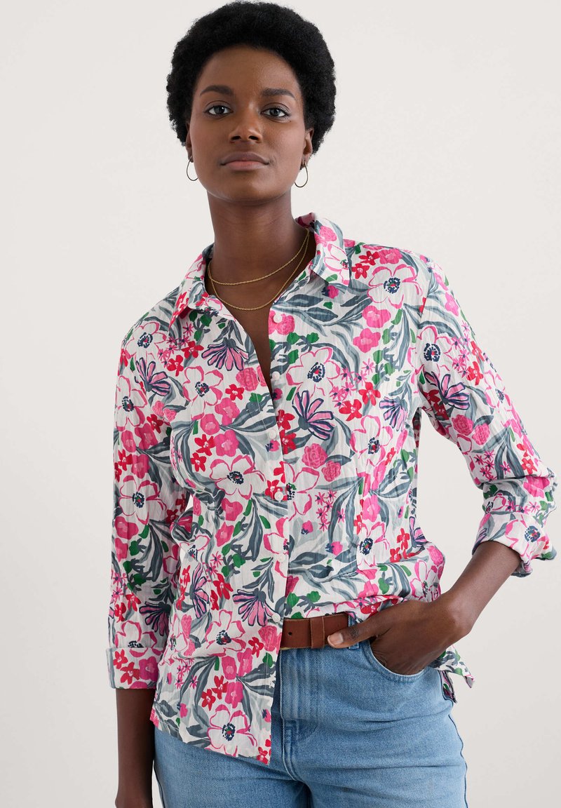 Blommönstrad skjorta i rosa, röd och grön nyanser. Tillverkad av ett lättviktigt tyg, har en krage och uppvikta ärmar.