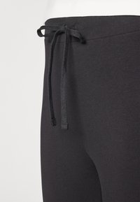 Pantaloni sportivi neri con cintura regolabile e tessuto liscio ed elasticizzato. Primo piano che mostra la trama e i dettagli delle cuciture tono su tono.