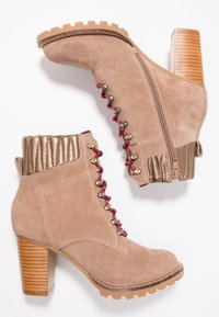 Beżowe zamszowe botki za kostkę z żłobionym, metalicznym, złotym kołnierzem, czerwonymi sznurowadłami, złotymi elementami i masywnym obcasem. Podeszwa z teksturowanej gumy dla lepszej przyczepności.