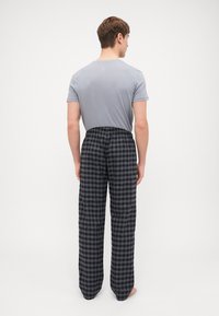Chemise grise à manches courtes associée à un pantalon à carreaux noirs et gris, avec une taille élastique et une coupe droite. Vue de dos.