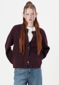 Violet knitted cardigan with a relaxed fit, featuring a round neck, long sleeves, and six black buttons on the front. Light cotton underneath.