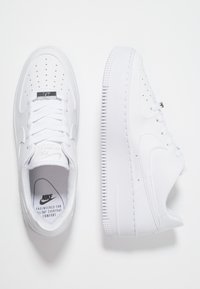 Para białych sneakersów Nike Air Force 1, jeden pokazujący górę z sznurówkami, drugi widok z boku z grubą podeszwą na białym tle.