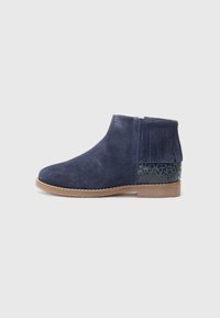 Bottine en suède navy avec une semelle plate en tan, ornée d'un accent frangé et d'un motif noir texturé sur le talon.