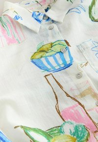 Chemise en lin blanc avec des imprimés abstraits colorés comprenant des bols de fruits, des bouteilles et des verres, dotée de boutons et d'un col.
