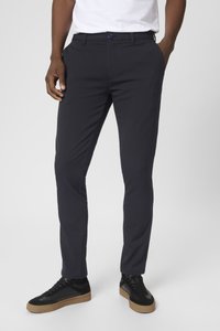 Pantalones ajustados azul marino, confeccionados en una tela suave, con cierre de botón y bolsillos laterales, combinados con zapatillas negras.