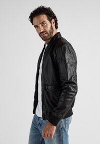 Schwarze Lederbomberjacke mit gerippten Bündchen und Saum, ausgestattet mit einem Reißverschluss und seitlichen Taschen. Glatte Textur und minimalistisches Design.