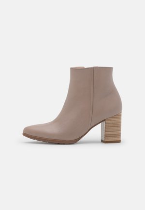 Bottine en cuir taupe avec talon bloc empilé et fermeture éclair latérale, bout arrondi élégant, design minimaliste sur fond blanc.