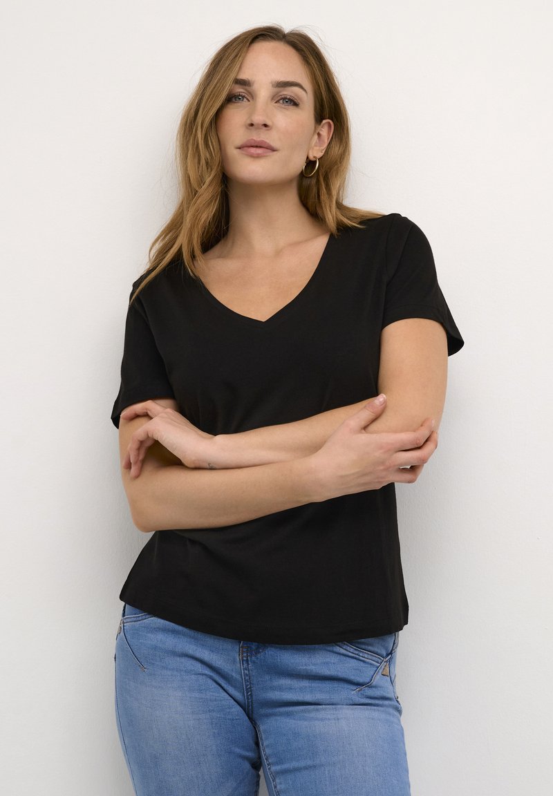 Melnās kokvilnas T-krekls ar V-veida kakla izgriezumu, īsām piedurknēm un brīvu piegriezumu. Apvienots ar gaiši ziliem džinsa biksēm, parādot neformālu tēlu.