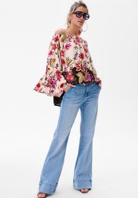 Blumenoberteil ohne Träger in Hellrosa mit lebhaften Blumen; kombiniert mit hellblauen Schlagjeans und schwarzen Sandalen. Sonnenbrille und kreisrunde Ohrringe.