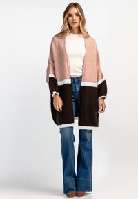 Sweter z dzianiny w kolorze różowym, brązowym i białym, z otwartym przodem i szerokimi rękawami. Połączony z dzwonowymi niebieskimi dżinsami i jasnym topem.