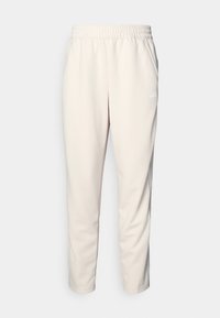 Helle beige Jogginghosen aus weichem Stoff, mit elastischem Bund und dezentem Logo-Detail am linken Oberschenkel.