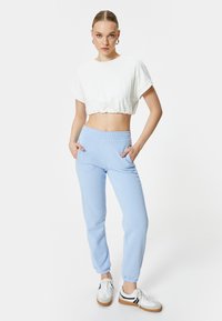 Witte cropped t-shirt met opgerolde mouwen, gecombineerd met lichtblauwe joggingbroeken met een elastische tailleband en zijzakken.