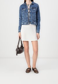 Blue denim jacket with silver buttons over a white ribbed dress. Brown handbag and leopard print flats with black straps complete the outfit.