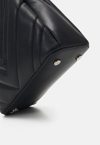 Czarna skórzana torebka z pikowanym wzorem, kanciastym kształtem i metalowymi nóżkami dla stabilności. Charakteryzuje się gładką fakturą i minimalistycznymi akcentami.