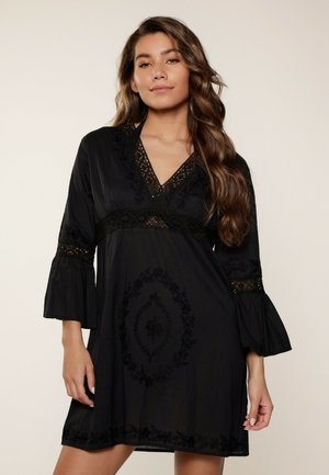 Robe noire avec un décolleté en V, des manches cloche et des broderies ornées. Fabriquée à partir d'un tissu léger avec une coupe décontractée et des accents en dentelle décorative.