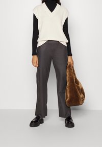 Cremig gerippter ärmelloser Pullover über einem schwarzen Rollkragenpullover, kombiniert mit grauen weiten Hosen und einer braunen Plüschtasche. Schwarze Plateauschuhe.