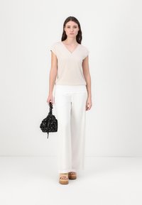 Svijetlosmeđi v-neck top u kombinaciji s bijelim širokim hlačama, sandalama na blok-petama i crnom torbom s uzorkom na vezanje.
