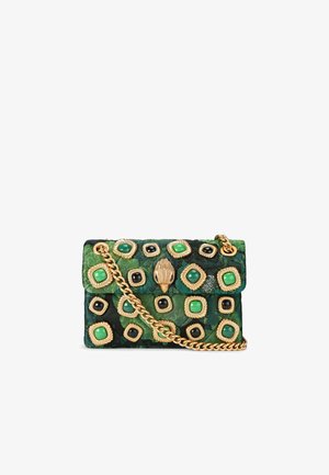 Borsa a tracolla in tessuto verde con catena dorata, decorata con pietre verdi, nere e dorate in un design a quadrato, su uno sfondo floreale testurizzato.