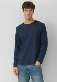 Marineblauw langarm T-shirt van zachte stof, met een ronde hals en een losse pasvorm, gecombineerd met lichtblauwe spijkerbroek.