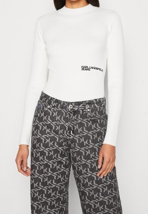 Weißes, geripptes Langarmshirt mit "Karl Lagerfeld Jeans"-Logo, kombiniert mit schwarzen und grauen, gemusterten Jeans mit ineinandergreifendem "KL"-Design.