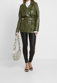 Chaqueta de cuero verde oliva de doble botonadura con bolsillos frontales y un cinturón, combinada con leggins de cuero sintético negros y un bolso de serpiente.