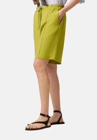 Pantaloni green lime con vita elastica e cordino, dotati di due tasche laterali e dal taglio dritto, abbinati a sandali neri.