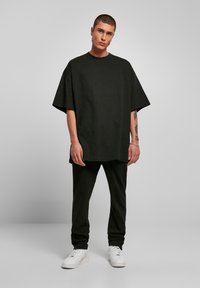 Zwarte oversized katoenen t-shirt met korte mouwen, gecombineerd met zwarte broek en witte sneakers, op een neutrale achtergrond.