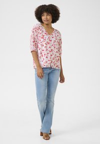 Blusa rosa a fiori con scollo a V e maniche a sbuffo, abbinata a jeans azzurri chiari e sandali con tacco a blocco marroni.
