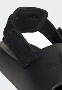 Black athletic sandals featuring adjustable Velcro strap, textured surface, and molded footbed with embossed logo detail.