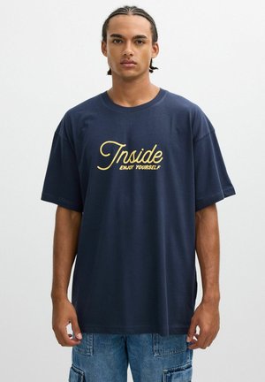 Camiseta oversized de color azul marino hecha de algodón, con un diseño de texto amarillo que dice "Disfruta de ti mismo por dentro" en la parte frontal.
