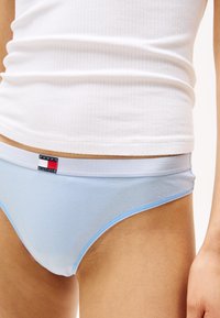 Lichtblauwe katoenen bikini slipjes met een contrasterende blauwe rand en een merkband met een logo in rood, wit en blauw.
