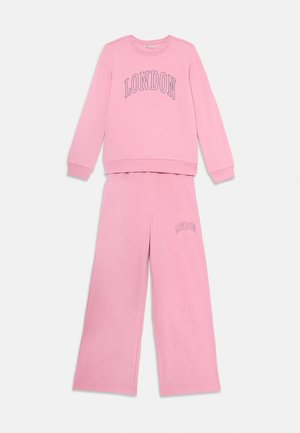 Rozā garās piedurknes džemperis un atbilstošas platas bikses, abiem priekšpusē ar uzrakstu "LONDONA" izklāstītās burtos.