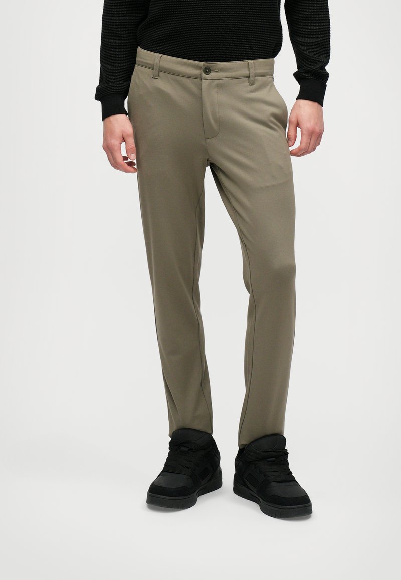 Ljusa olivgröna byxor i slätt material, med knäppning och två sidofickor. Stylar med svarta sneakers.