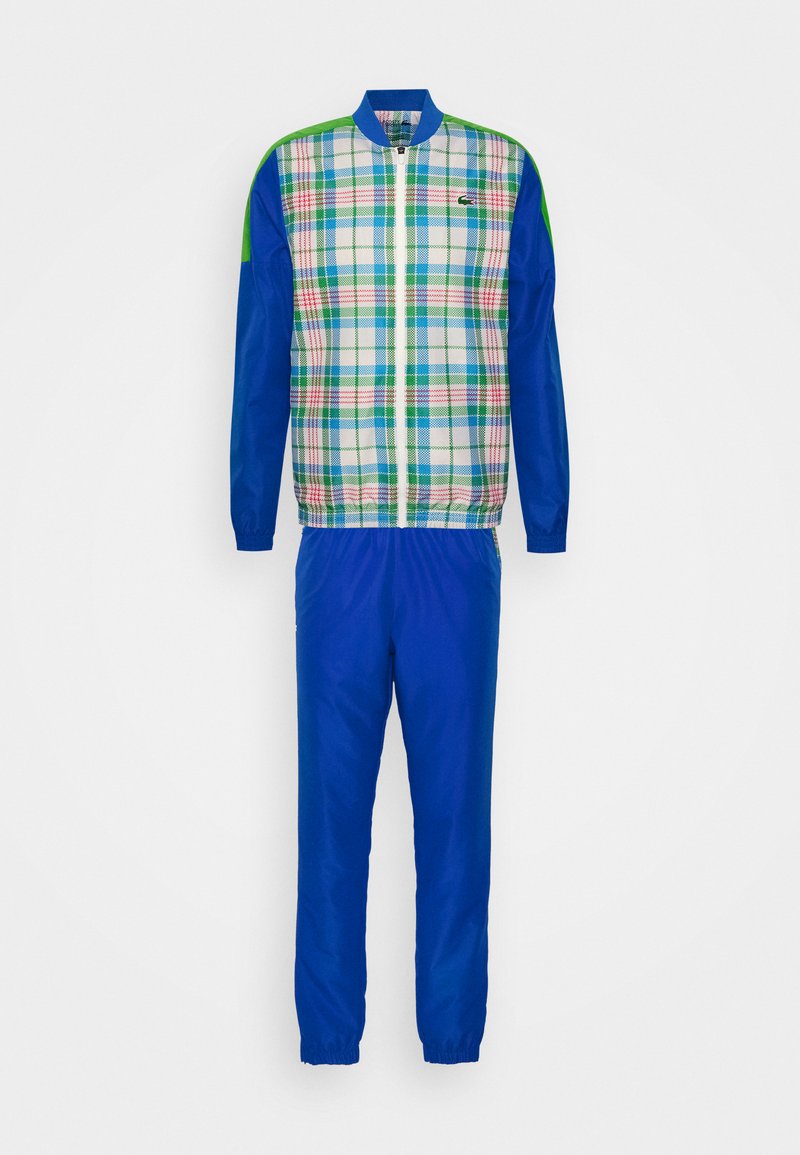 Ensemble de survêtement comprenant une veste à carreaux aux couleurs bleue, verte et blanche, associée à un pantalon bleu uni, le tout fabriqué dans un matériau lisse.