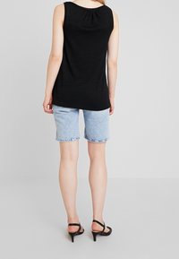 Haut noir sans manches avec une coupe décontractée, associé à un short en denim bleu clair et des sandales noires à talons. Design simple, style décontracté.