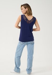 Top senza maniche blu navy con una schiena in pizzo a forma di V, abbinato a jeans a gamba larga blu chiaro e sneakers bianche. Tessuto dalla consistenza liscia.