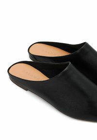 Černé kožené muly s hladkým povrchem, otevřenou zadní částí a minimalistickým designem. Podešev je elegantní s světle hnědou stélkou s embosovaným logem.