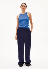 Blue ribbed tank top paired with navy loose-fit trousers; fabric appears smooth, with an elastic waistband, and casual footwear with fringe details.