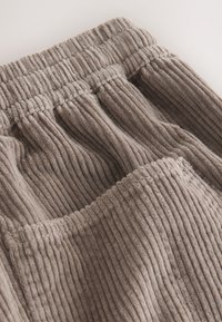 Cordhosen in weichem Braun mit vertikal geripptem Muster, ausgestattet mit einem elastischen Bund und einer großen Fronttasche.