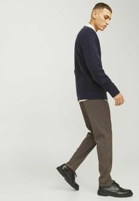 Marineblauer Strickpullover mit Rippenstruktur, kombiniert mit braunen gerade geschnittenen Hosen und schwarzen Schnürschuhen. Modell geht zur Seite.