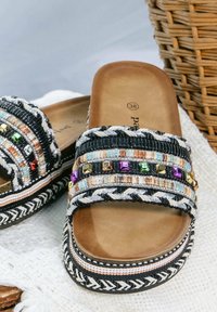 Infradito con una soletta color cuoio, cinturini intrecciati neri e bianchi con perline colorate e dettagli metallici, e una suola intrecciata.