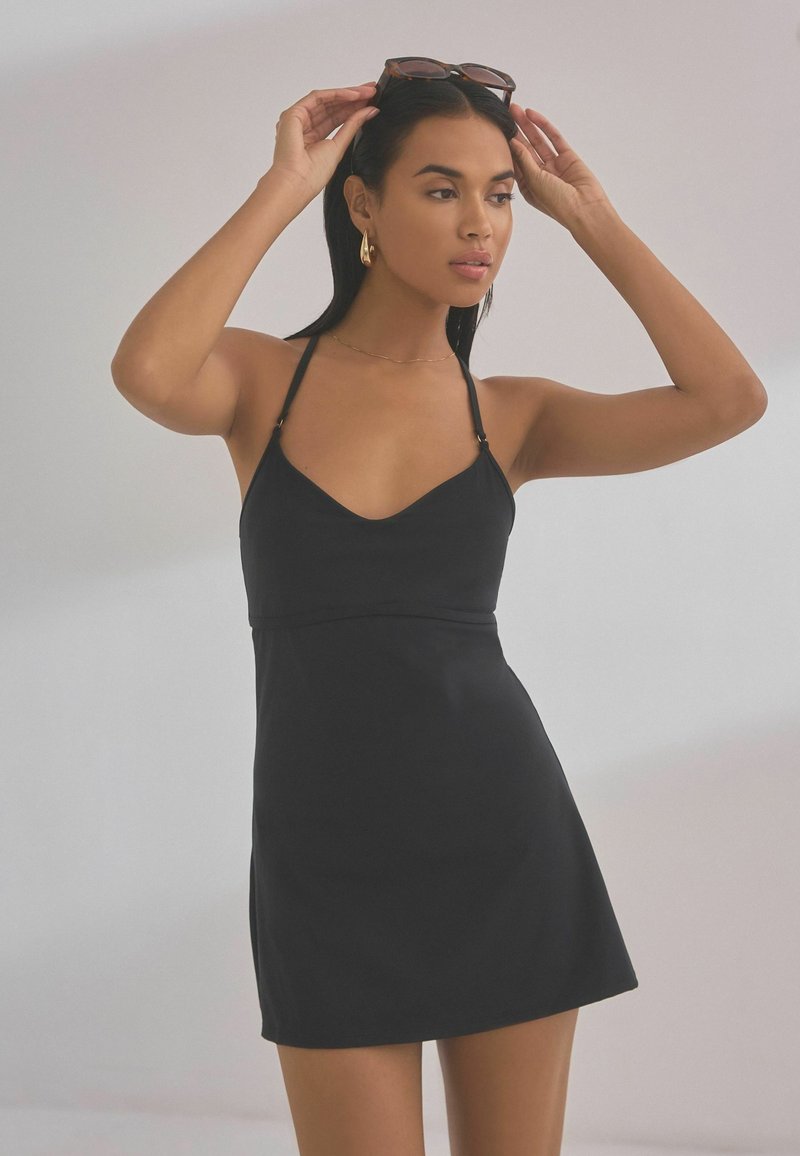 Zwarte slip jurk met een V-hals, verstelbare bandjes en een getailleerde taille. Glad materiaal en knielange snit. Accentueert door gouden hardwaredetails.
