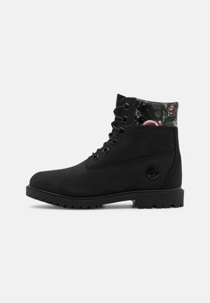 Botte noire à lacets avec semelle épaisse et col matelassé à motif floral, avec logo arbre embossé sur le côté.