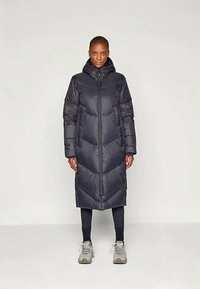 Dolg, temen pufast plašč s kapuco, ki ima ševron šiv, sprednji zadrgo in stranske žepe. Teksturovan material z gladkim zaključkom.