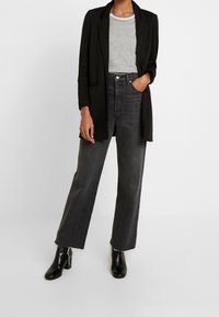 Schwarze Blazer über einem grauen T-Shirt, kombiniert mit hoch taillierten, geraden, dunkelblauen Jeans und schwarzen Blockabsatz-Stiefeletten.