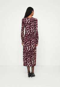 Haljina dugih rukava boje burgundca s kremastim uzorkom u spirali, izrađena od rastezljivog materijala, s okruglim izrezom i dizajnom do gležnjeva.