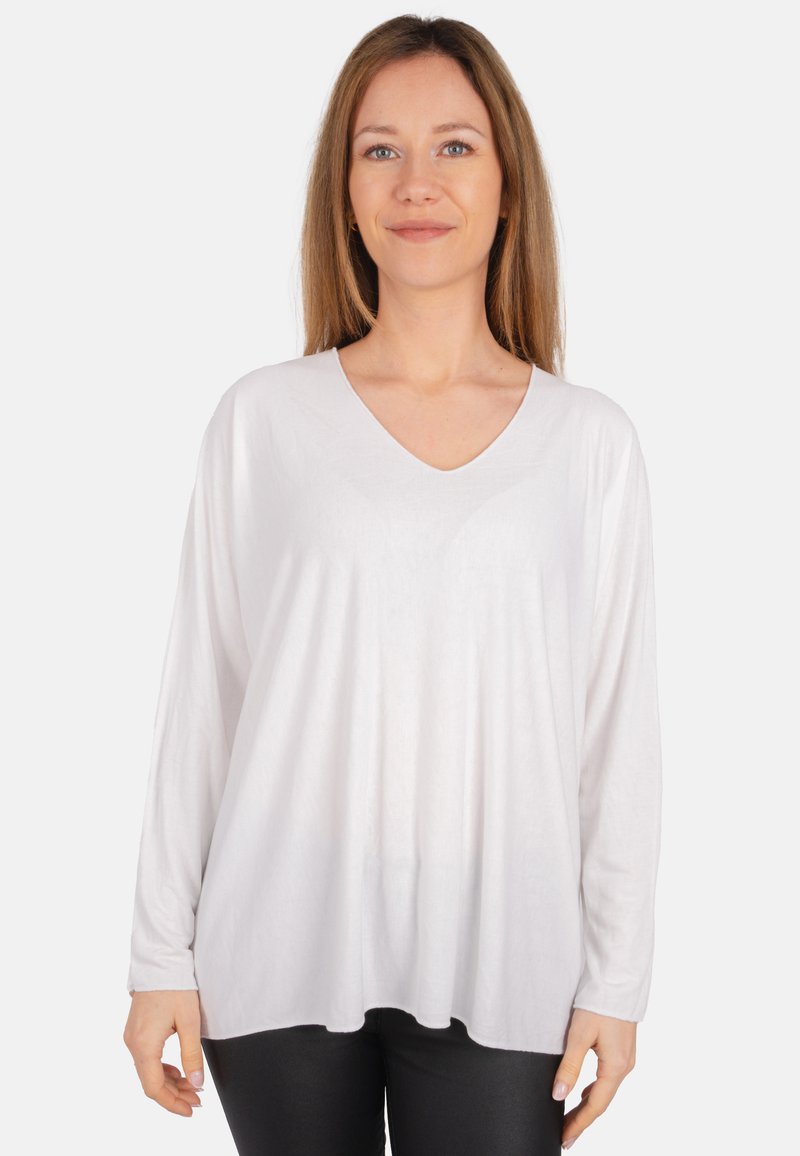 Weißes Longsleeve-Oberteil mit V-Ausschnitt und lässiger Passform. Weicher, leichter Stoff mit glatter Textur. Kombiniert mit schwarzen Hosen.