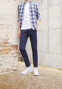 Camicia a quadri blu e bianca, t-shirt bianca, pantaloni navy e sneaker bianche. Tessuto liscio, design aderente, posa in piedi.